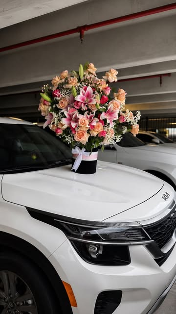 Pink rose arrangement placed on the hood of a white car as a surprise